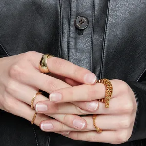 Detailaufnahme einer Hand mit geschichteten Goldkettenringen und einem glatten Ringband