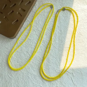 Primo piano di collane di perle di spinello giallo brillante su sfondo bianco strutturato.