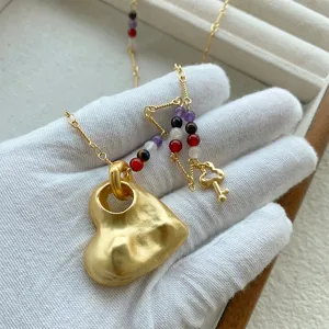 Primo piano di una collana a cuore dorato 3D con perle colorate e ciondolo a chiave.