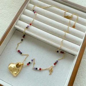 Dettaglio di una collana con pendente a cuore testurizzato dorato e perline colorate