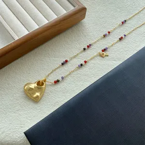 Dettaglio di una collana con ciondolo a cuore dorato materico e perline colorate