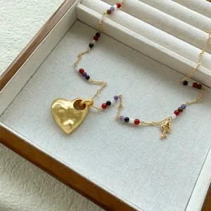 Primo piano del ciondolo a cuore dorato testurizzato e perline colorate su una collana.