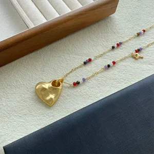 Primo piano del ciondolo a cuore dorato strutturato e perline colorate su collana lunga