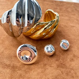 Hochglänzende klobige Armreifen und Ohrstecker in Gold und Silber auf Wildleder.