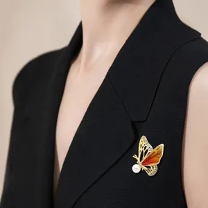 Detail van een emaille vlinderbroche met strass en parel op een stijlvolle zwarte blazer
