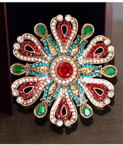 Détail d'une broche baroque vintage ajourée avec strass colorés sur monture dorée.