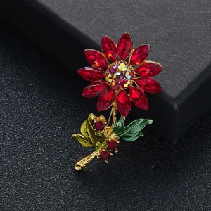 Detailopname van een zonnebloem broche met rode strass steentjes en groene bladeren.