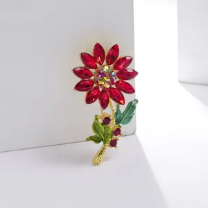 Gedetailleerd overzicht van een elegante zonnebloem speld met rode kristallen en bladeren