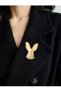 Detailansicht einer goldenen Vintage-Hasenbrosche an einem schwarzen Wollmantel.