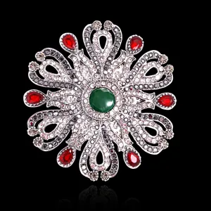 Broche baroque vintage avec pierre verte centrale et gouttes rouges sur fond noir.