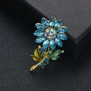 Detail van een zonnebloem broche met sprankelende blauwe strass en groene bladeren