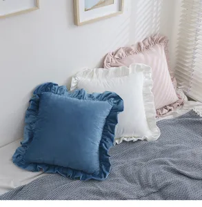 Detailansicht der Volantkanten von blauen, weißen und rosa Samtkissenbezügen auf dem Bett.