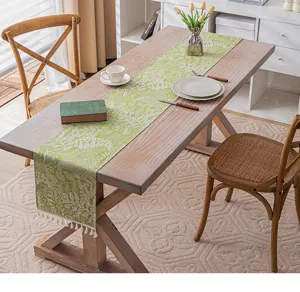 Frischer grüner Tischläufer mit Blumenmuster und Quasten auf einem rustikalen Holztisch.