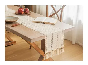 Detailed view of a beige hand-woven table runner with delicate fringe and hollow-out pattern.