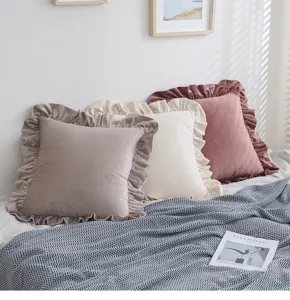 Drei Samtkissen mit Rüschenrand in Altrosa, Creme und Taupe auf einem weichen Bett.