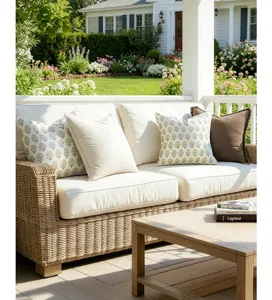Vintage floral and solid throw pillows on a wicker sofa in a sunny garden porch setting