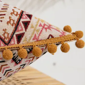 Detailed view of ethnic style woven pillowcase with mustard yellow pom-pom trim