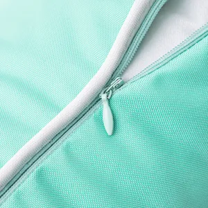 Detalle de funda de cojín turquesa impermeable para exterior con ribete blanco y cremallera.