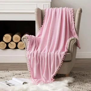 Manta de franela rosa suave con ribete de pompones decorativos sobre un sillón beige