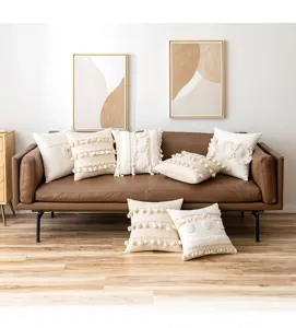 Detailed view of boho decorative cushion covers with tassels and pom-poms on a leather sofa