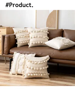 Detailed view of cream bohemian cushion covers with tassels and pompoms on a brown sofa