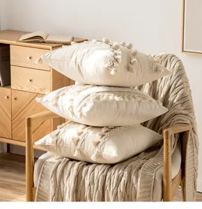 Stack of cream boho throw pillow covers with decorative tassels and pompoms on chair