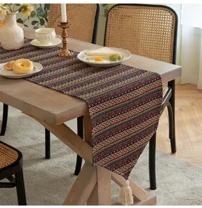 Runner da tavola boho con motivi a rombi colorati e nappe su un tavolo di legno rustico