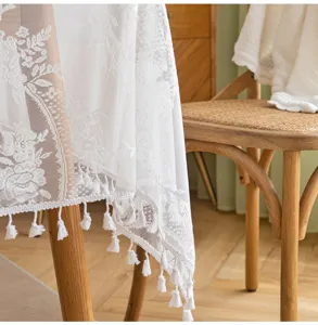 Close-up detail of white French lace tablecloth with elegant floral patterns and tassels.