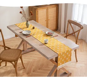 Detalle de camino de mesa de algodón amarillo con motivos de estrellas y flecos en madera