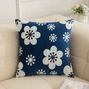 Funda de cojín azul marino con bordado floral blanco en un sofá crema