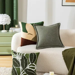 Housses de coussin vert artistique avec motifs de feuilles et pied-de-poule sur canapé.