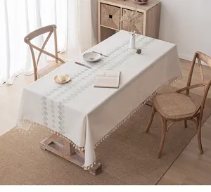 Cream embroidered tablecloth with tassels displayed on a wooden dining table