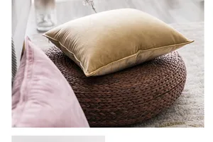 Close-up detail of a soft yellow velvet pillowcase on a woven pouf in a cozy room.