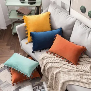 Fundas de cojín de terciopelo de colores con borlas en un sofá gris con manta beige.