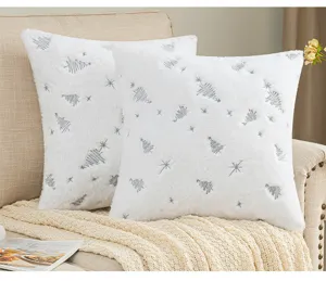 Detail of white plush Christmas pillow covers with silver tree embroidery on a sofa.