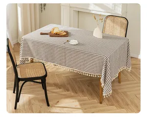 Detailed view of brown checkered tablecloth with tassels on a wooden dining table