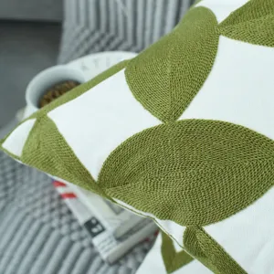 High-quality close-up of green geometric leaf embroidery on white linen pillow cover.