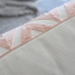 Détail macro d'une broderie géométrique rose sur une housse de coussin de style crème