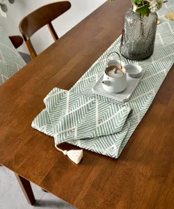 Vue détaillée d'un chemin de table jacquard vert et blanc avec pompon sur bois foncé