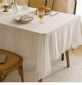Close-up of white pastoral lace tablecloth with delicate floral embroidery on a wooden table.