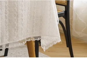 Detailed close-up of white floral lace tablecloth with scalloped embroidered edges.