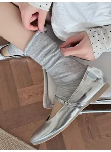 Detail shot of grey scrunched leg warmers paired with metallic silver flats on wooden floor.
