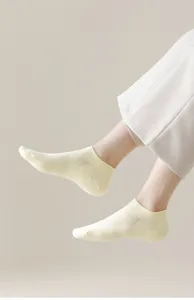 Close-up shot of light yellow mesh short socks worn with white trousers in studio.