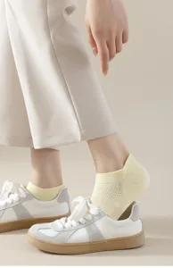 Close-up detail of breathable mesh low-cut boat socks in soft yellow, worn with casual sneakers.