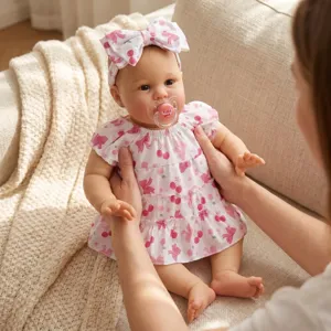 Lifelike 22-inch reborn baby doll Ellie wearing a cherry print dress on a sofa