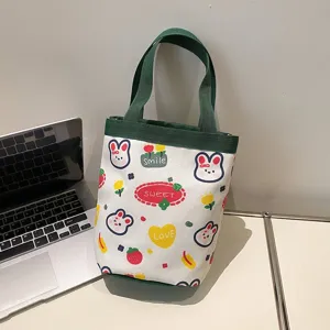 Small cute Japanese style cartoon canvas lunch bag shown next to a silver laptop