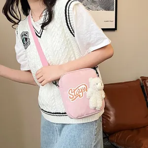 Primer plano de un bolso bandolera de nailon rosa con un adorable amuleto de oso blanco.