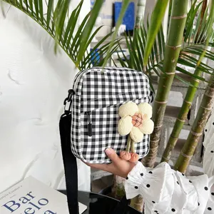 Detalle de un mini bolso bandolera a cuadros blancos y negros con colgante de flor de peluche.