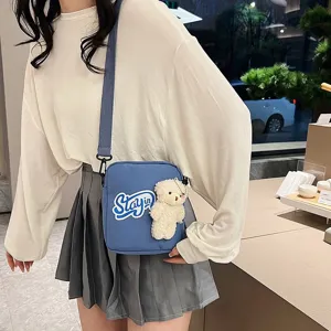 Detalle de bolso bandolera de nailon azul con oso de peluche y parche de Stay-in