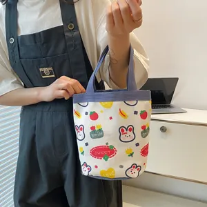 Detail view of a cute cartoon canvas tote bag with rabbit prints held by a person.